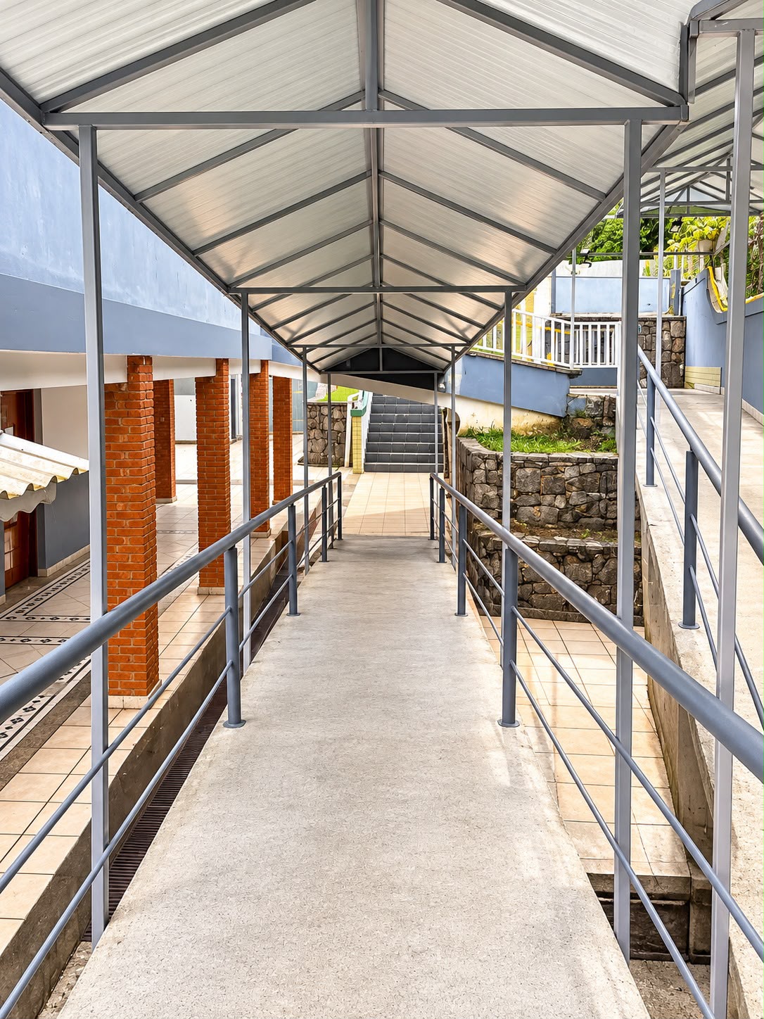 Passagem coberta da unidade com corrimãos laterais.